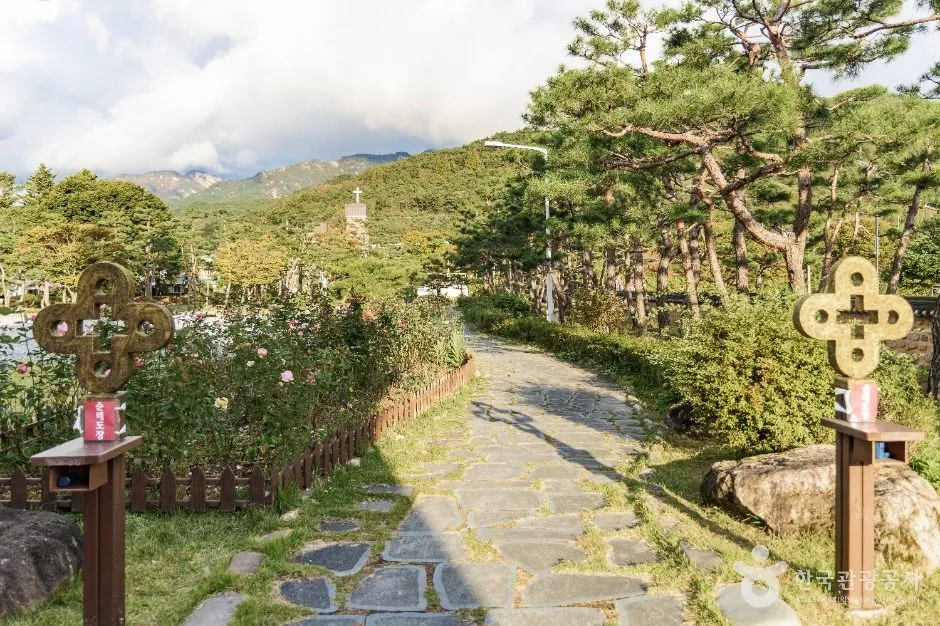 연풍성지 꽃밭 사이로 난 돌길과 양옆의 십자 문양 표지 기둥