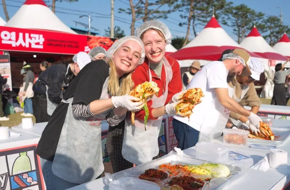 괴산 김장축제 체험장에서 위생모·앞치마 차림 참가자들이 버무린 김치를 들어 보이는 모습, 뒤로 빨간 지붕 천막