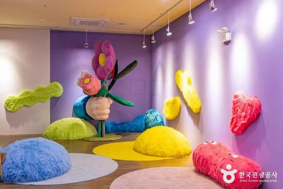 보라색 벽 전시실 바닥에 놓인 털실 질감의 알록달록한 조형물들 — 괴산생태뮤지엄 별별탐사대 전시